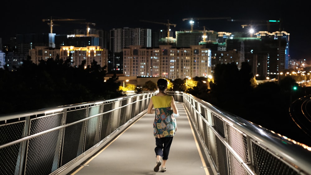 woman in green jacket and black skirt walking on bridge during night time
