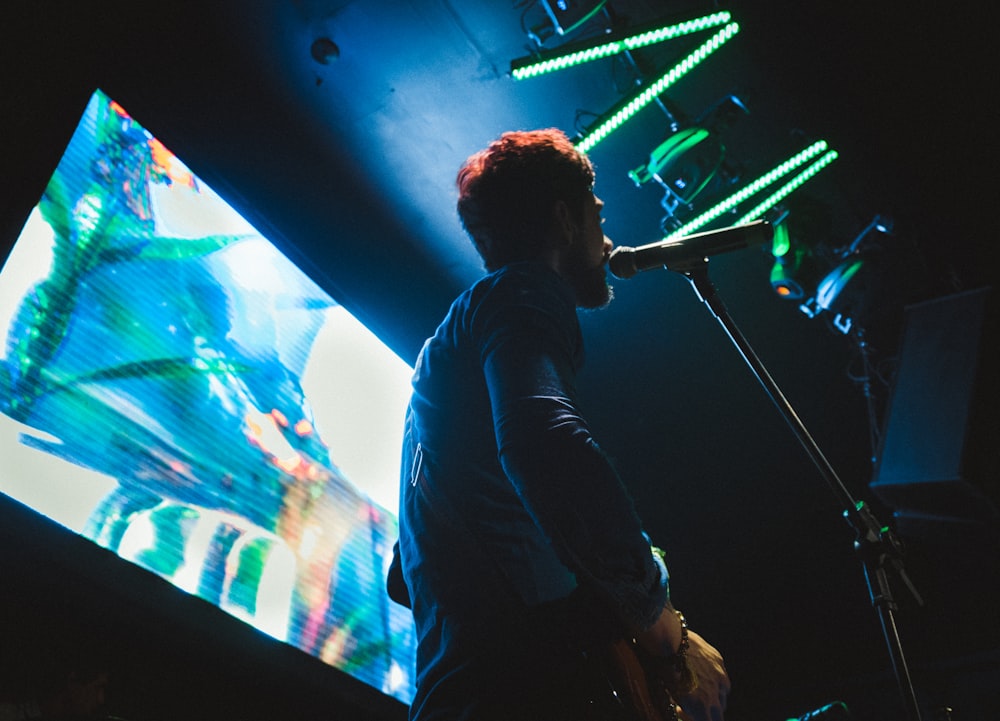 man in black long sleeve shirt standing in front of blue and green lights