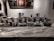 An array of coffee brewing equipment is displayed on a marble countertop. There are several different types of coffee makers, including pour-over and siphon coffee makers, as well as containers and jars filled with coffee beans. Behind the counter, decorative artwork featuring abstract patterns and figures adorns the wall. The ambiance is enhanced by low, warm lighting.