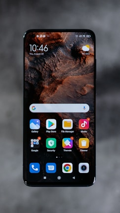 A smartphone displaying a home screen with various app icons, including Gallery, Play Store, File Manager, and Music. The background features a textured, earthy design. The time reads 10:46 and the date is displayed as Thursday, August 20. The top right corner shows a weather widget with a sun icon and a 'No data' label.