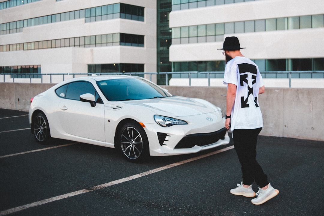 man in white and red t-shirt and black pants standing beside white mercedes benz coupe