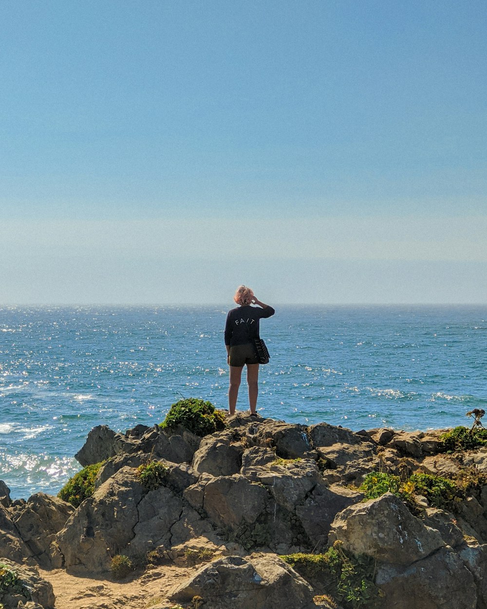 donna in abito nero in piedi sulla formazione rocciosa vicino al mare durante il giorno