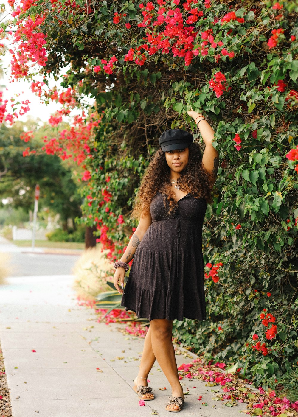 woman in black dress standing near red flowers during daytime