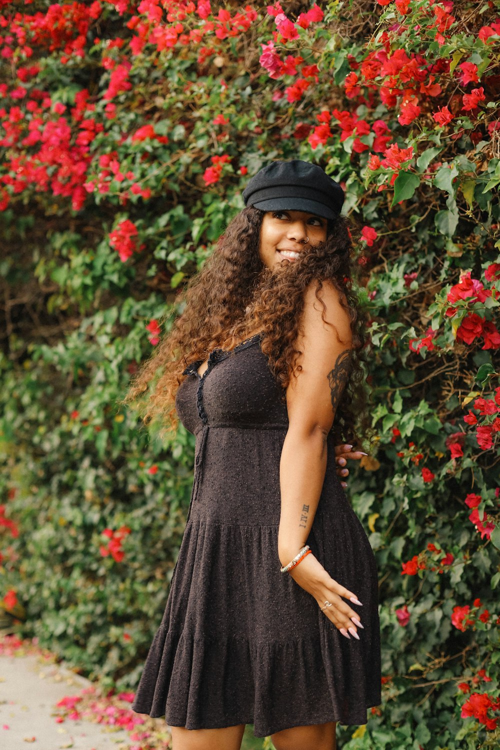 woman in black spaghetti strap dress standing near red flowers