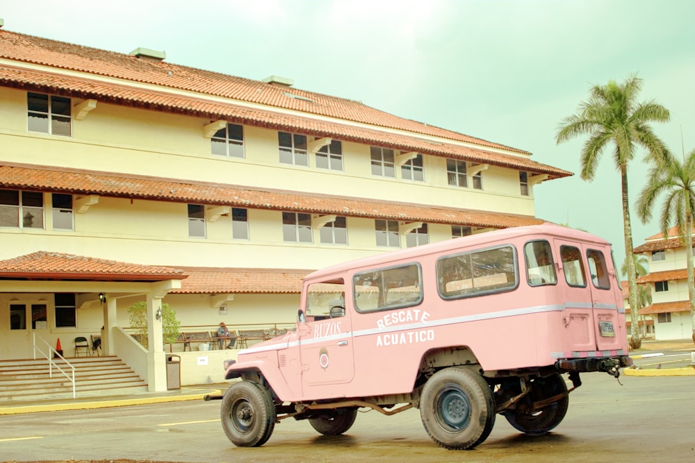 pink and white vintage car parked in front of white and brown concrete building during daytime