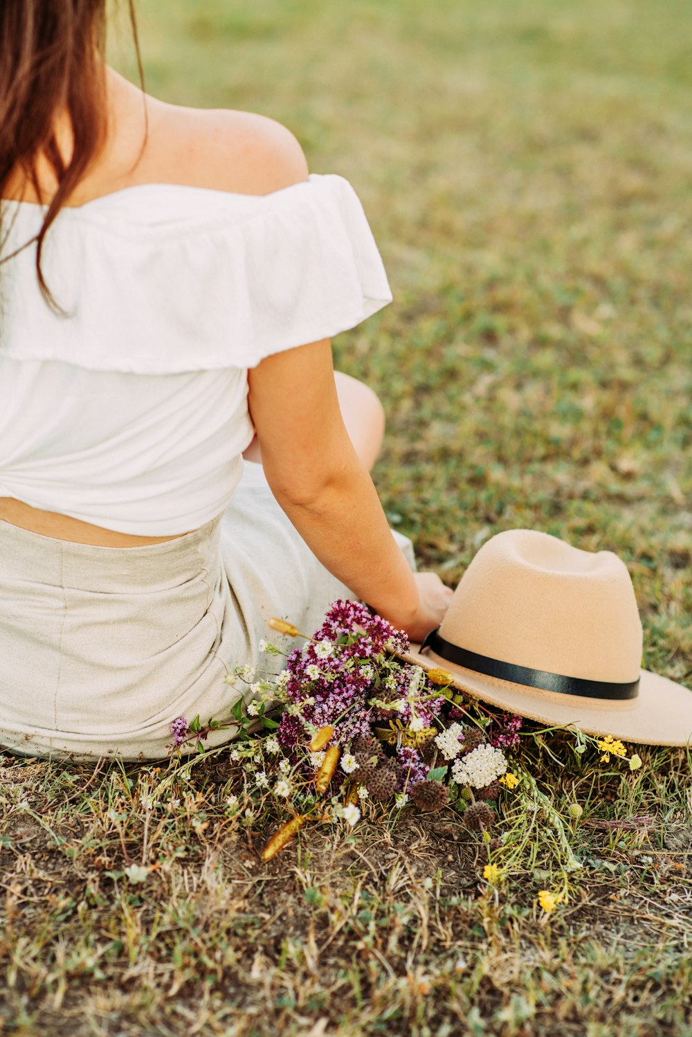 woman in white shirt and white skirt wearing brown hat sitting on green grass field during
