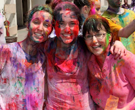 A joyful group of friends playing Holi, splashing bright colors in the air against a soft gradient background.