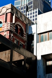 A mix of architectural styles is evident in the urban setting, with a classic red brick building featuring arch windows and decorative stone elements juxtaposed against modern glass and steel structures. The scene captures the harmony and contrast between historical and contemporary architecture.