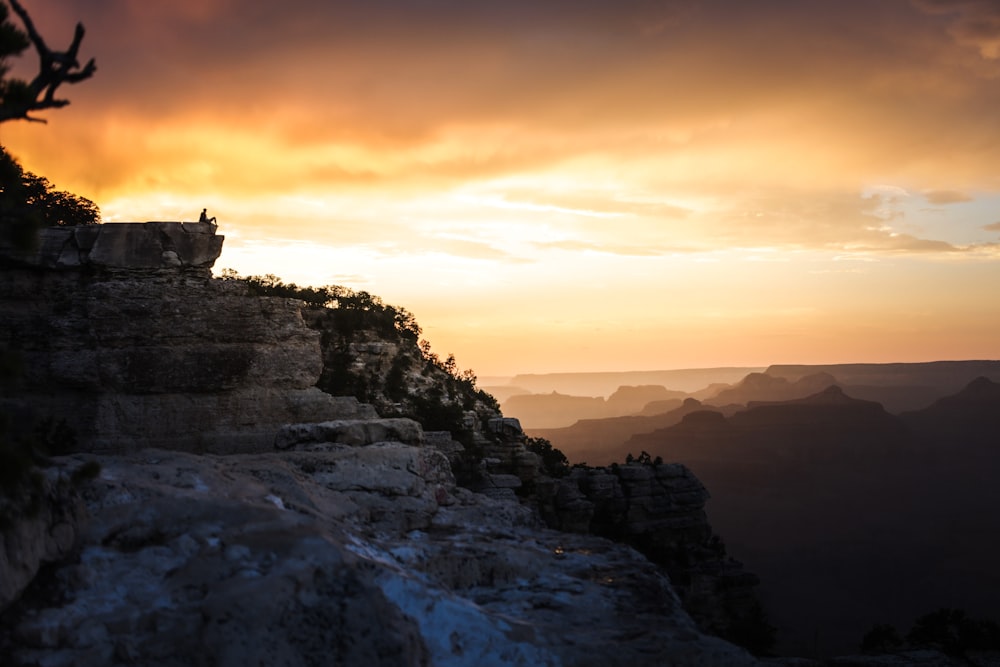 silhouette of person standing on rock formation during sunset