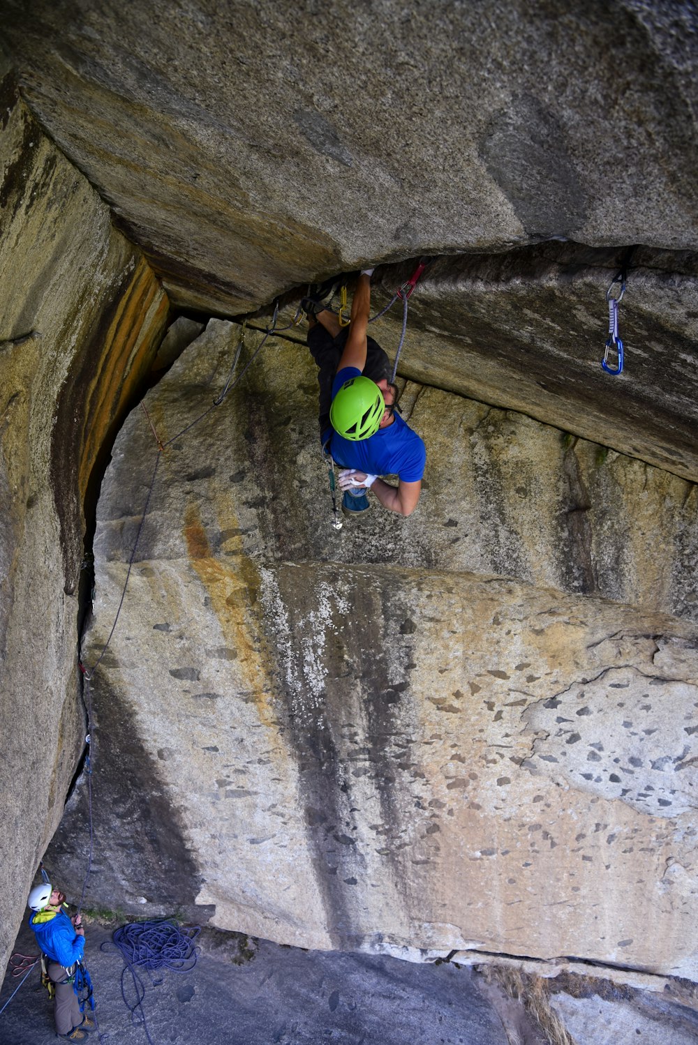 man in blue tank top climbing on brown rock