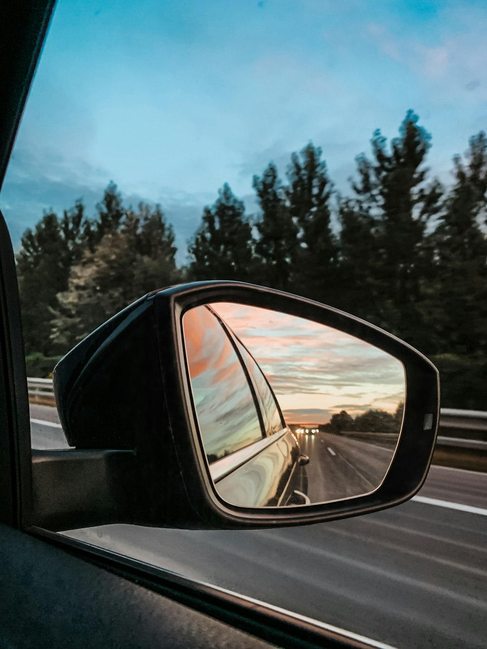 Espejo lateral del automóvil que muestra el automóvil en la carretera durante el día