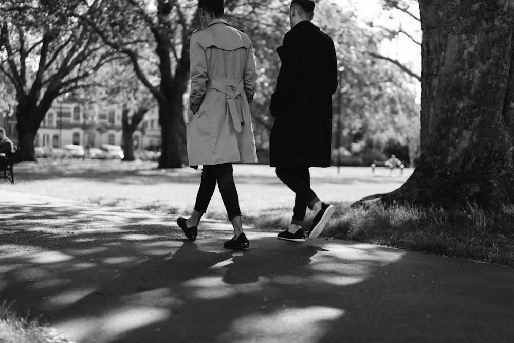 grayscale photo of woman in coat and pants walking on road