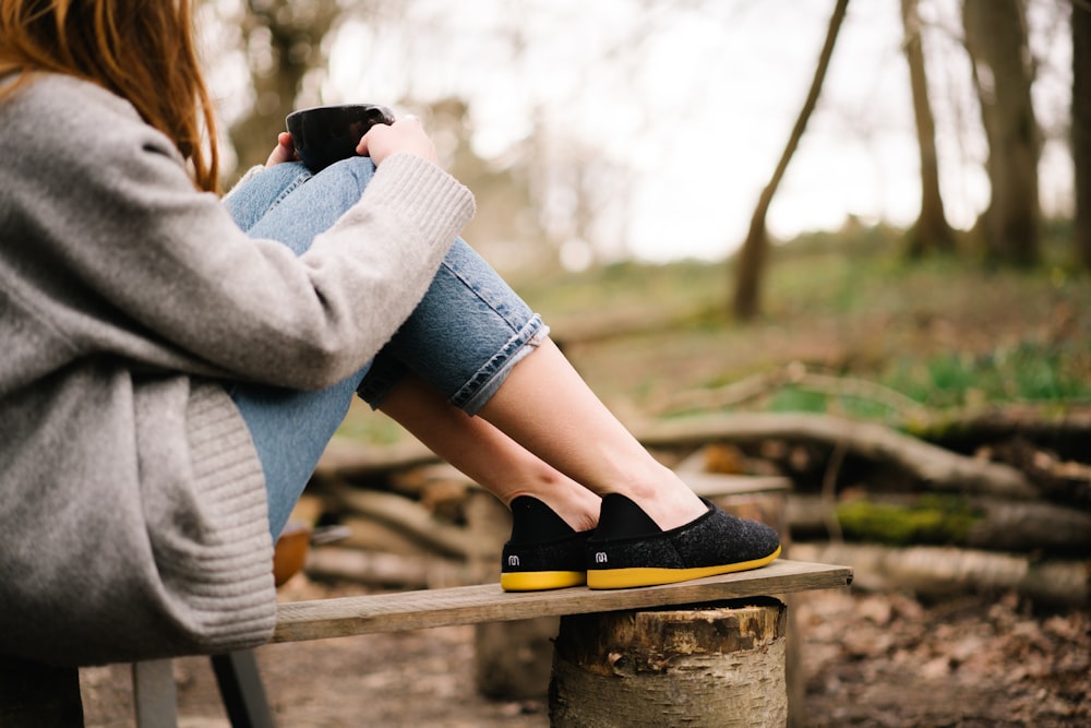 woman in gray sweater and blue denim shorts sitting on brown wooden bench during daytime