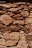 A rustic stone wall is constructed with irregularly shaped and sized rocks, tightly fitted together. The stones exhibit a range of earthy tones, with visible textures and weathering marks, suggesting an aged structure. Light and shadow interplay across the surface, highlighting the rough and uneven surface of the stones.