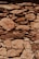 A rustic stone wall is constructed with irregularly shaped and sized rocks, tightly fitted together. The stones exhibit a range of earthy tones, with visible textures and weathering marks, suggesting an aged structure. Light and shadow interplay across the surface, highlighting the rough and uneven surface of the stones.