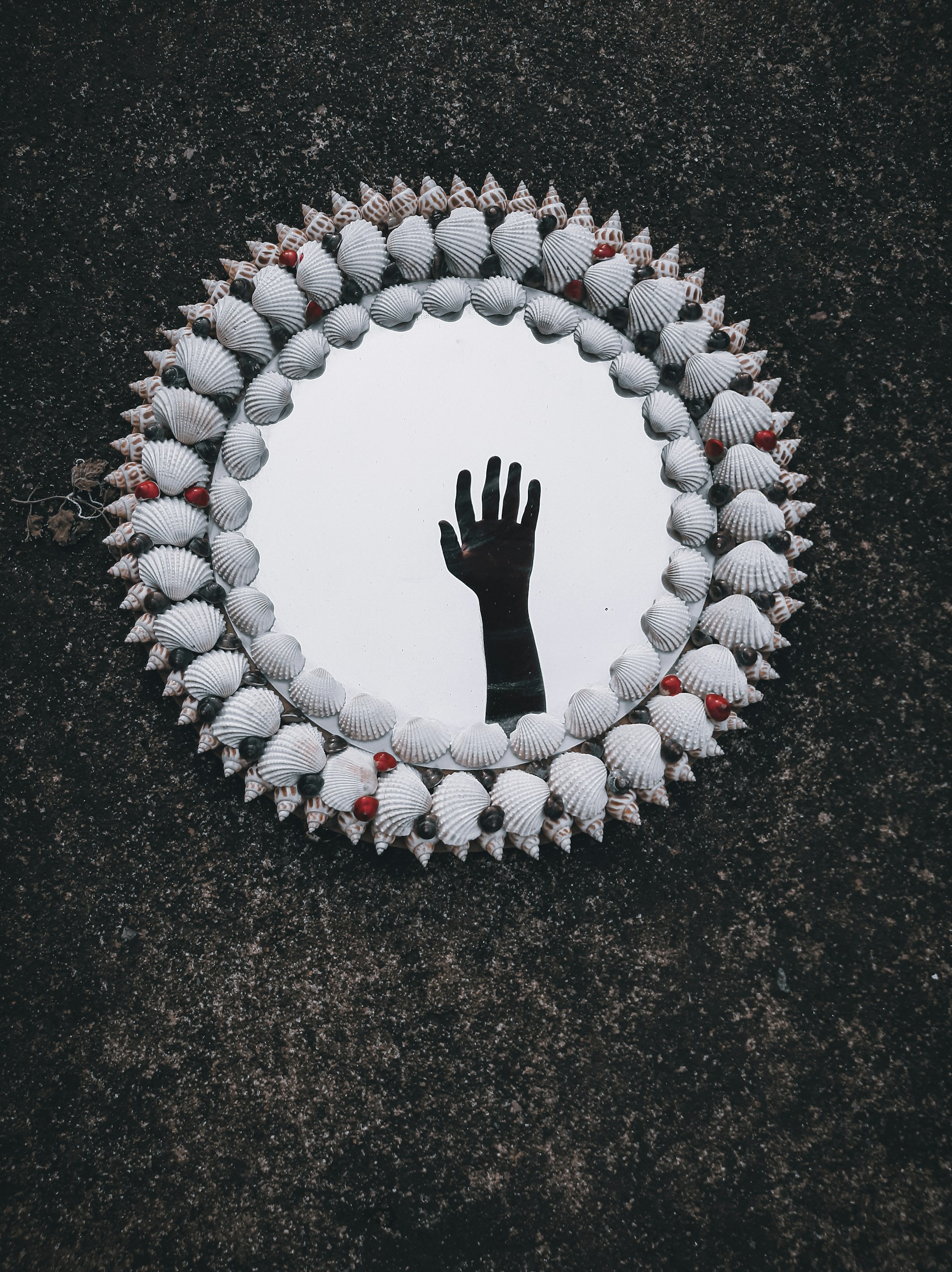 A romantic hand mirror featuring intricate seashell designs, displayed on a dark red velvet surface.