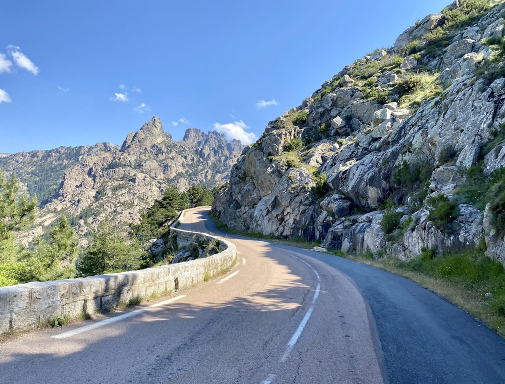 gray concrete road near green and gray mountain under blue sky during daytime