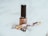 A beige nail polish bottle with a black cap is placed on a soft white fabric. Nearby, there is an ornate fountain pen with floral designs and gold accents. The scene suggests a subtle elegance and minimalistic aesthetics.