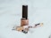 A beige nail polish bottle with a black cap is placed on a soft white fabric. Nearby, there is an ornate fountain pen with floral designs and gold accents. The scene suggests a subtle elegance and minimalistic aesthetics.