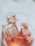 A hand with manicured nails holds a glass bottle of Coco Mademoiselle Chanel perfume. The bottle has a transparent cap and a golden neck. The liquid inside appears amber or rosy in color.