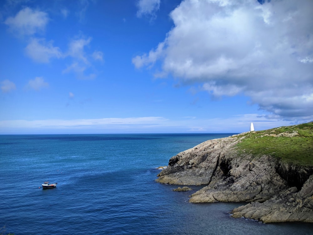 white and brown lighthouse on top of hill by the sea under blue and white cloudy