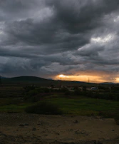 A vast apocalyptic landscape under a stormy sky lit by distant, fiery glows.