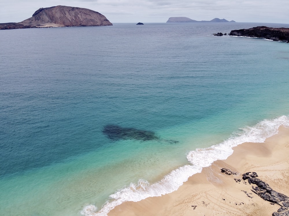 brown sand beach with ocean waves crashing on shore during daytime