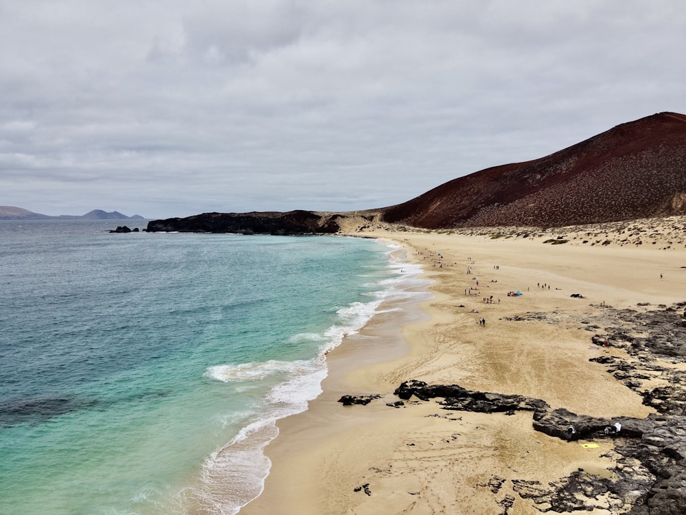 Plage de sable brun avec des vagues d’eau verte sous les nuages blancs et le ciel bleu pendant la journée