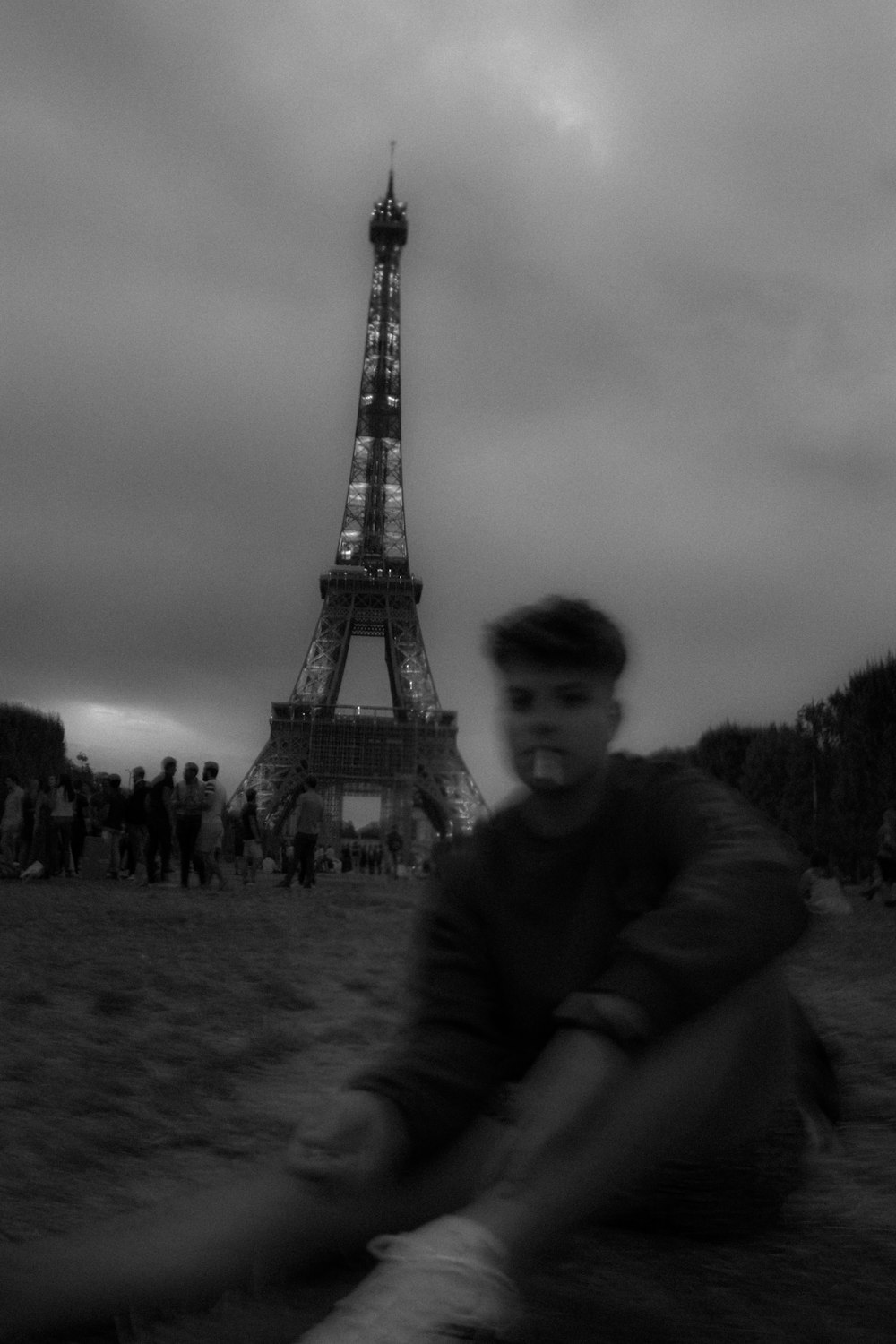 grayscale photo of man in sweater sitting on ground near eiffel tower