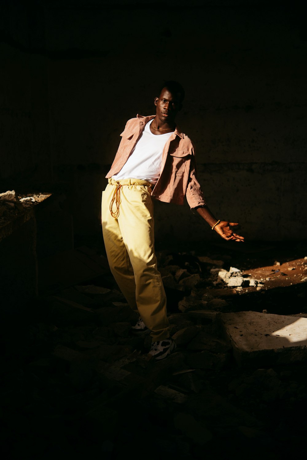 homem na camisa branca de manga comprida e calças amarelas em pé no chão de concreto cinza