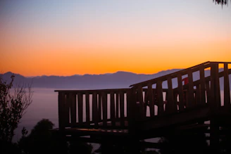 A beautifully crafted multi-level deck with curved railings overlooking a lush backyard at sunset.