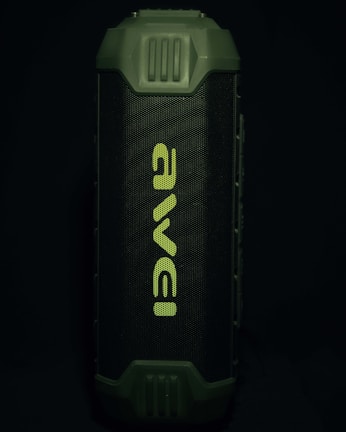 A portable speaker with a rugged, green exterior and a prominent front grille displaying the brand name in a stylized font. The design appears durable and suitable for outdoor use.