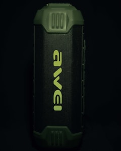 A portable speaker with a rugged, green exterior and a prominent front grille displaying the brand name in a stylized font. The design appears durable and suitable for outdoor use.