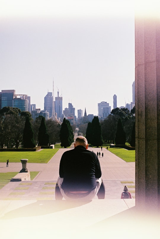 man in black shirt sitting on white bench during daytime in Shrine of Remembrance Australia