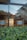 A modern architectural interior is seen through a window. There are two minimalist wooden benches with light blue cushions. The window reflects a partially visible urban skyline and trees. The interior features large open spaces with a glossy floor and contemporary design elements.