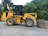 A yellow front loader vehicle with large tires is parked on a gravel surface, surrounded by dense green foliage and hills in the background. The machine has a prominent logo on the side, indicating the brand 'Liugong'.