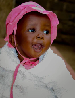 A playful baby wearing a soft hat and cozy clothes, smiling joyfully.