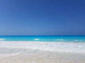 Pristine white sandy beach with turquoise waters gently lapping the shore under a clear blue sky.