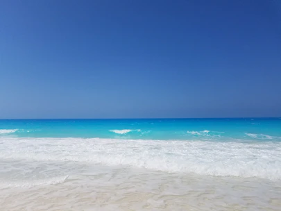 Pristine white sandy beach with turquoise waters gently lapping the shore under a clear blue sky.