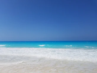Pristine white sand beach with turquoise waters gently lapping the shore under a clear blue sky.