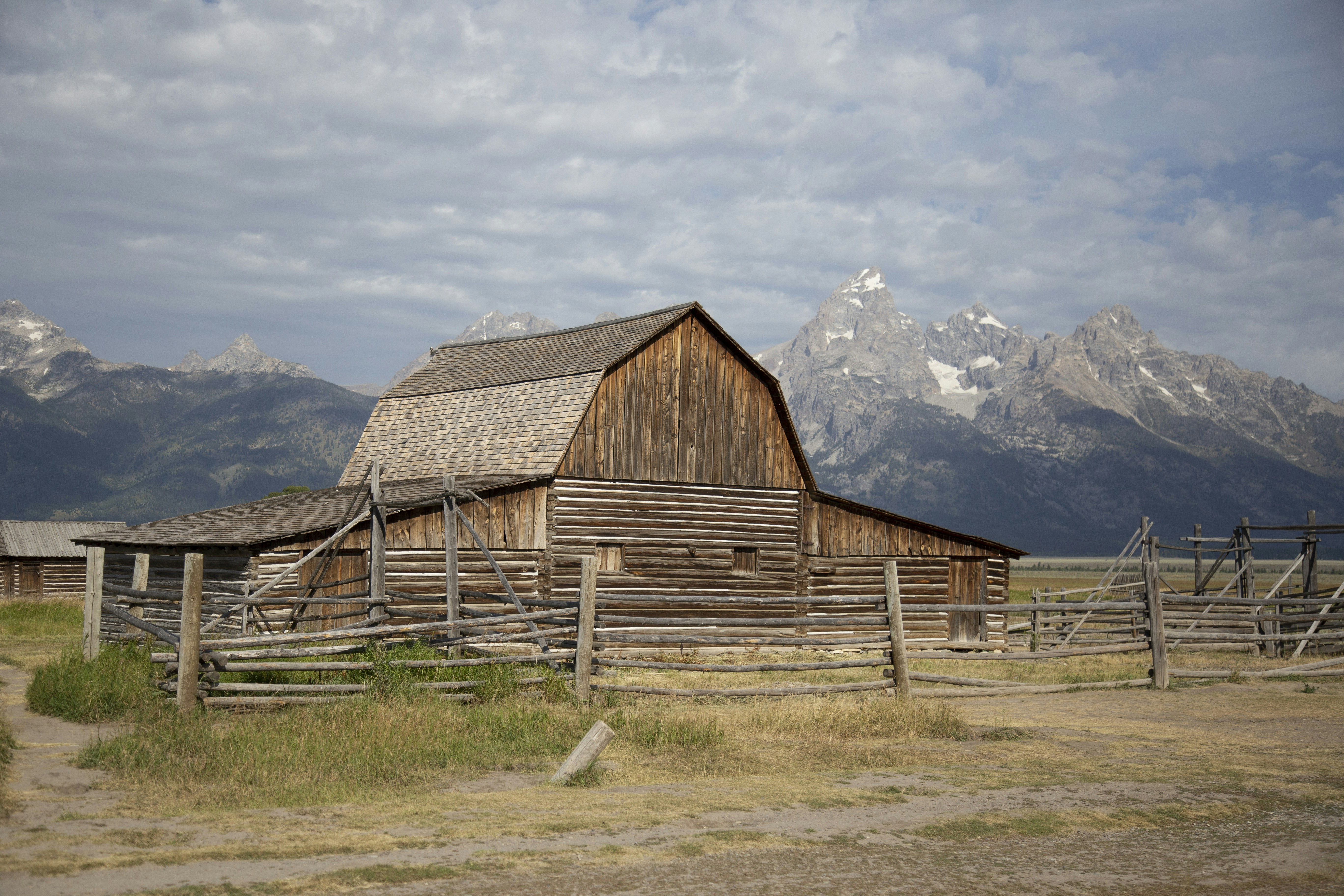 brown wooden barn on green grass field near mountains under white clouds during daytime