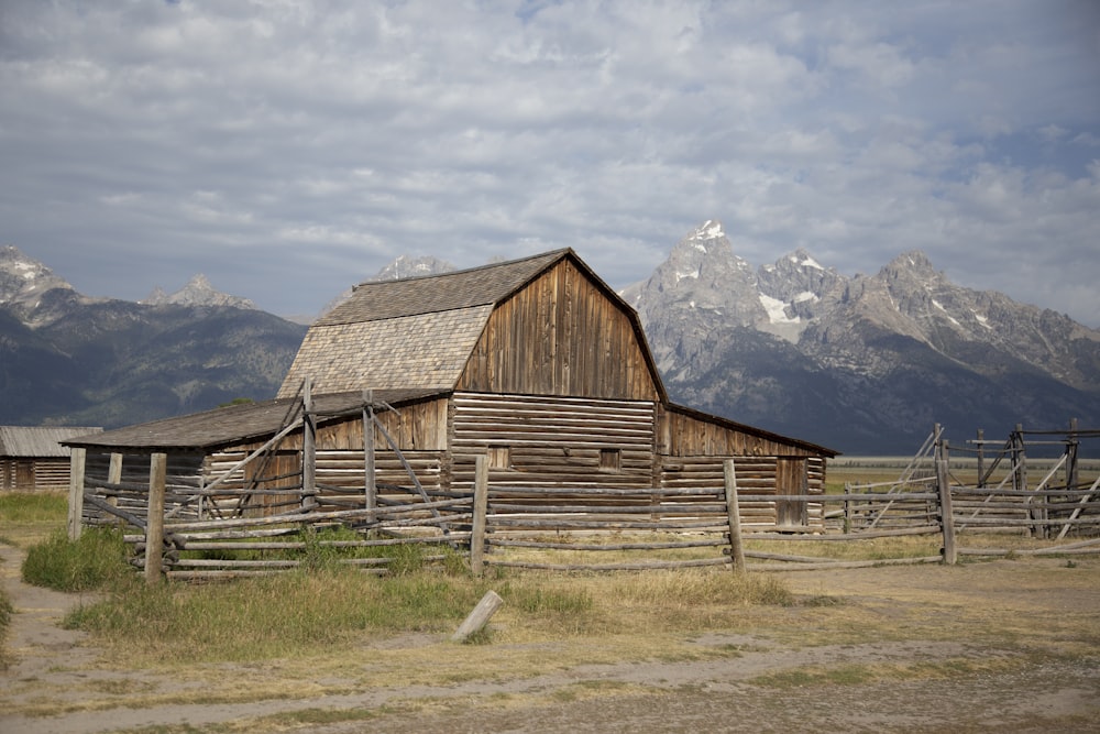 brown wooden barn on green grass field near mountains under white clouds during daytime