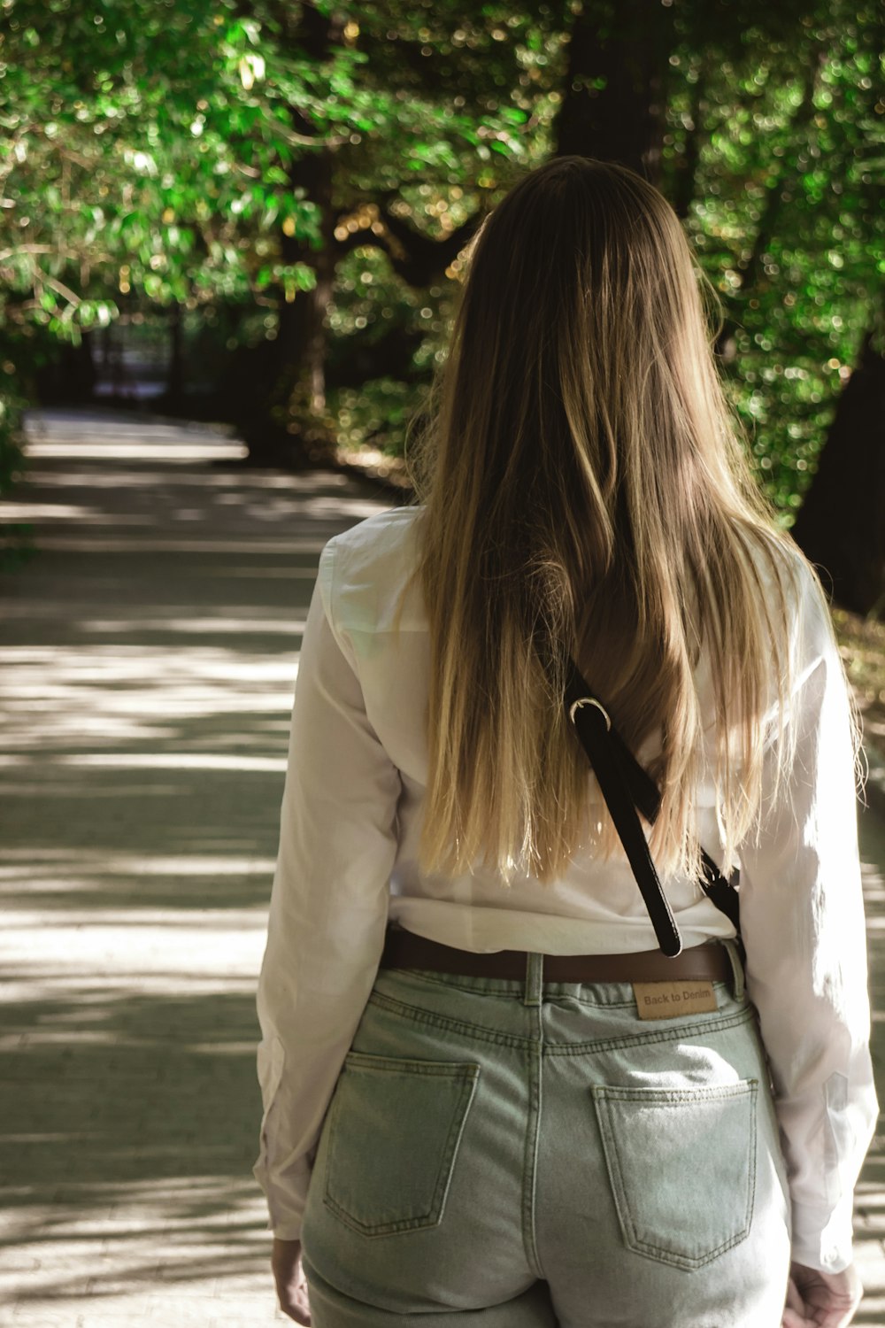 woman in white long sleeve shirt and gray denim jeans standing on sidewalk during daytime