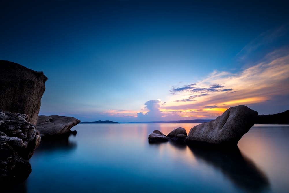 gray rock formation on body of water during sunset