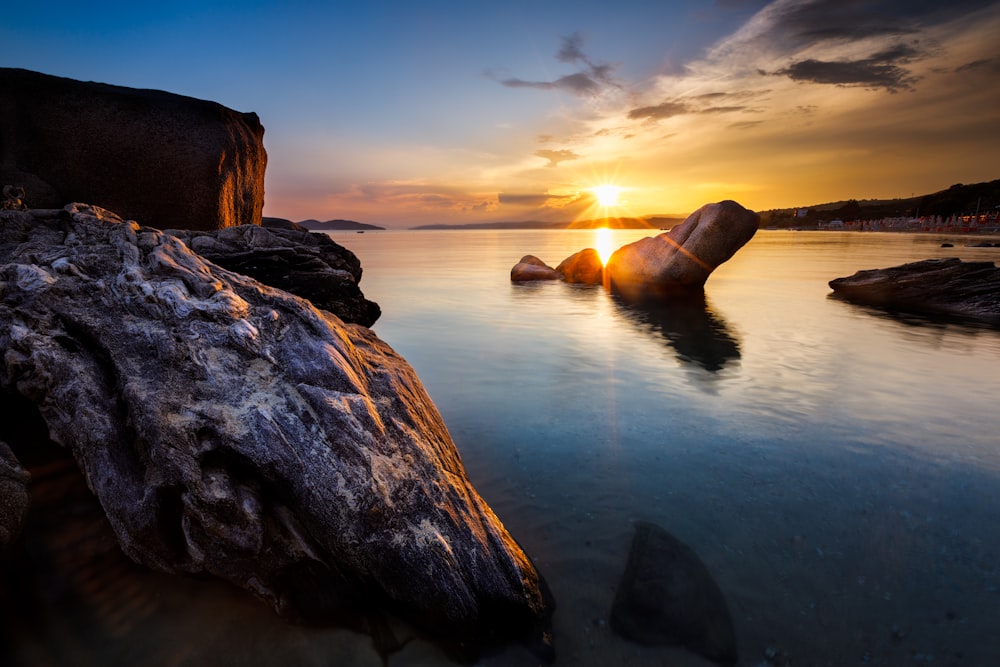 brown rock formation on body of water during sunset