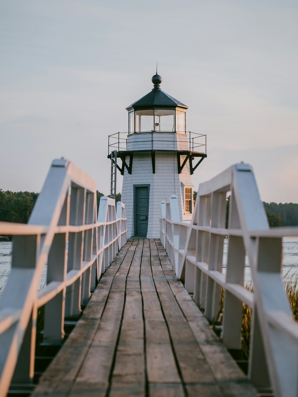 white wooden dock near white and red lighthouse under white sky during daytime