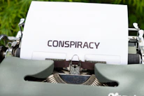 A monochrome typewriter with a sheet of paper showing classified dossier-style text.