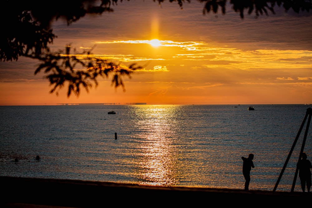 silhueta da pessoa em pé na praia durante o pôr do sol