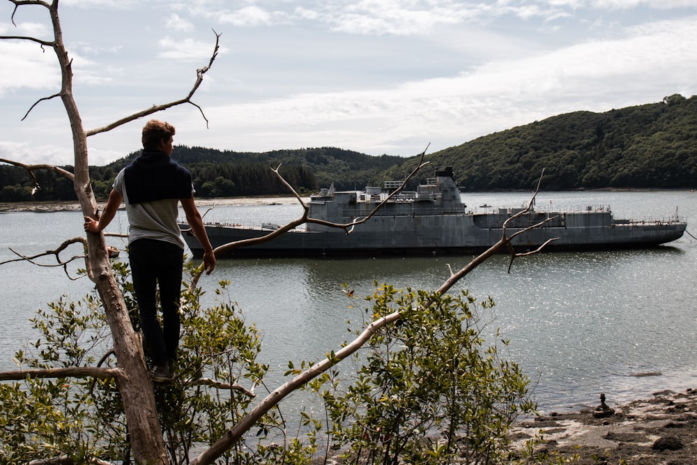 man in white shirt and black pants standing on brown tree branch near body of water