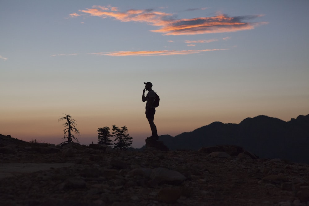 silhouette of man standing on rocky ground during sunset